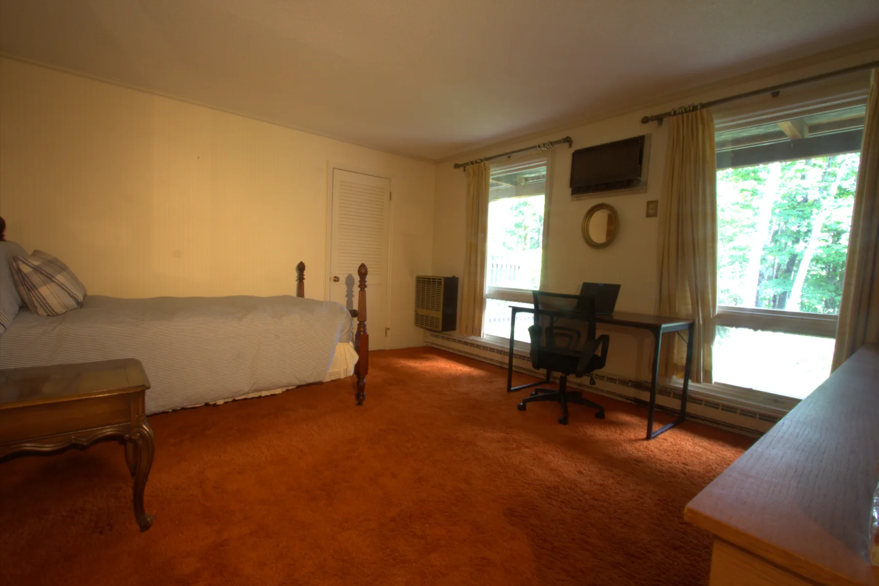 A bedroom with a writing desk and forest views