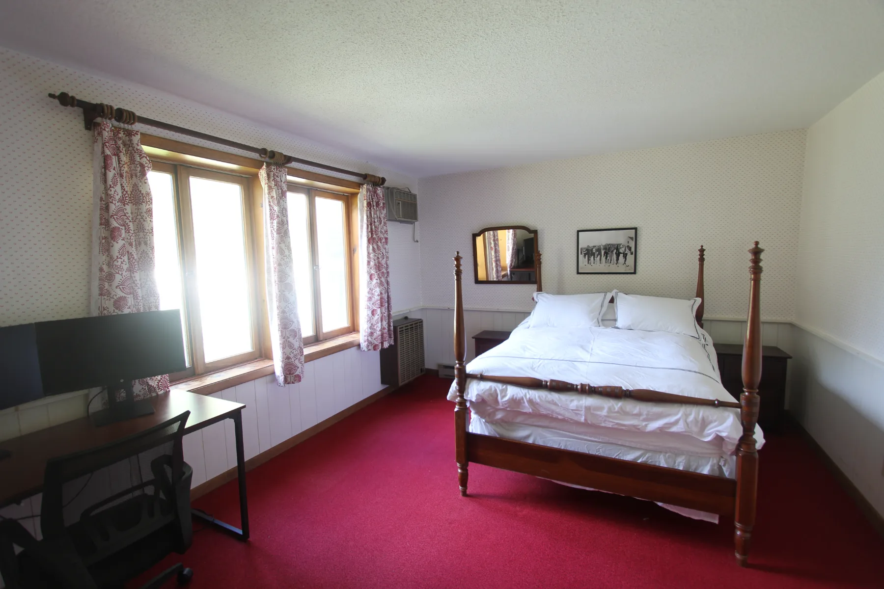 A red-carpeted bedroom with a four-poster bed and desk
